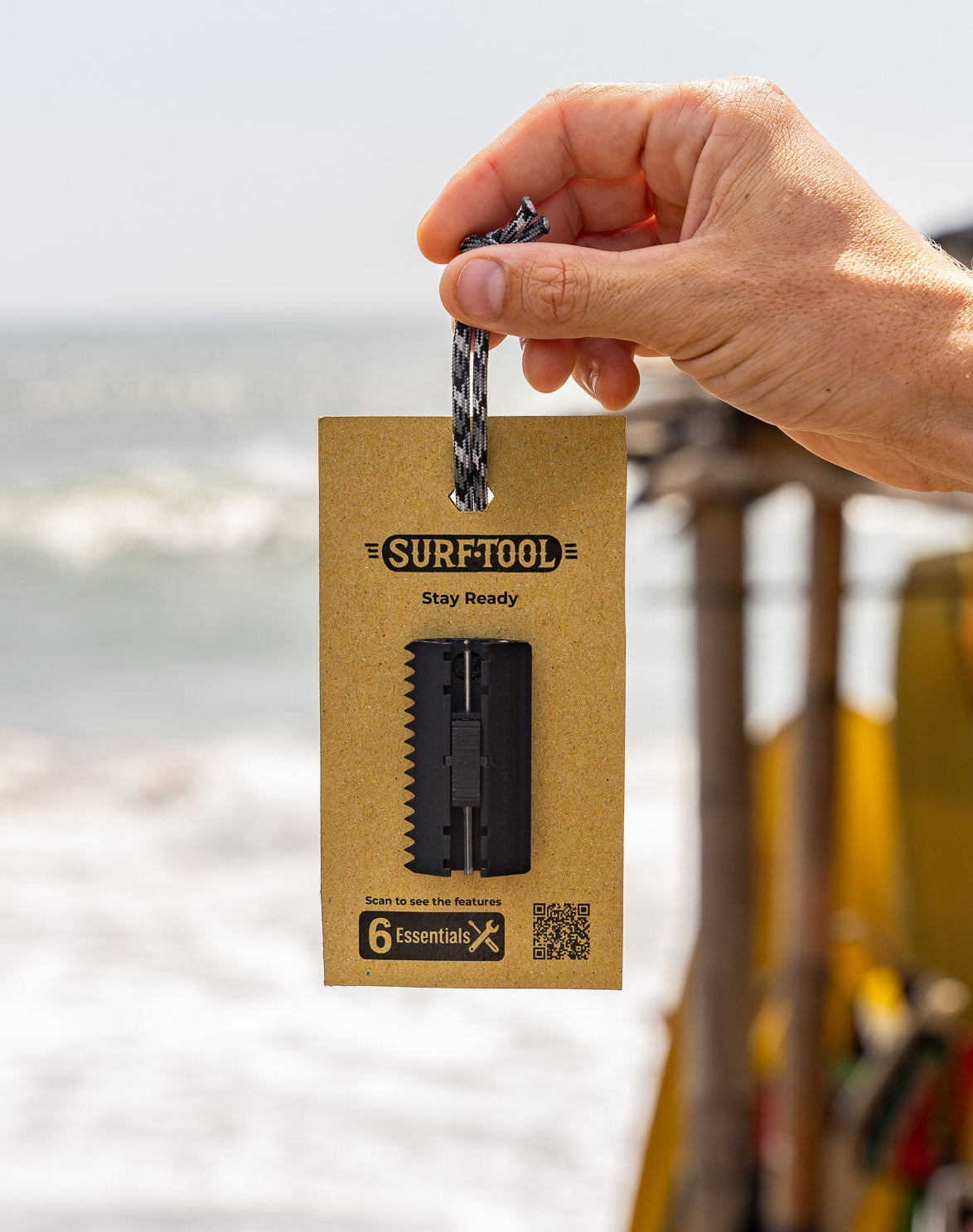 Hand holding a keychain with a 'Surftool' packaging on a beach background